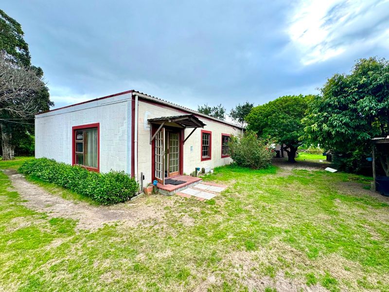 Rear view of a single-story concrete block house featuring timber-framed windows and a small entrance awning, set within a spacious garden area.