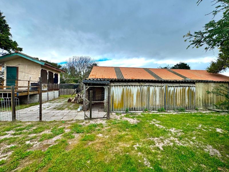 Rear view of the property featuring a large outbuilding with corrugated metal cladding and roofing, adjacent to a paved patio and fenced yard area.