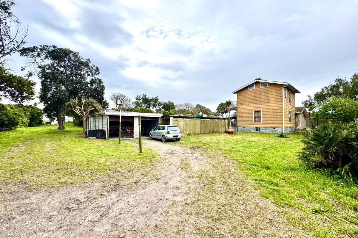 Rear view of the property featuring a detached garage, timber-clad dwelling, and a large grassed yard with an unpaved driveway.