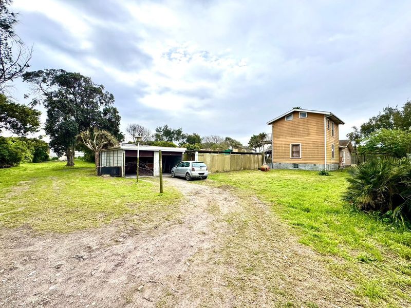 Rear view of the property featuring a detached garage, timber-clad dwelling, and a large grassed yard with an unpaved driveway.