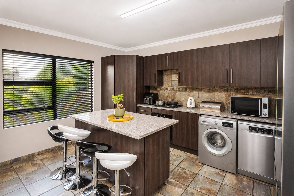 Modern kitchen featuring dark wood cabinetry, granite countertops, stone tile backsplash, and a functional kitchen island with integrated appliances.