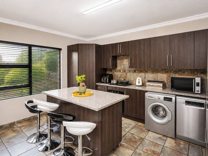 Modern kitchen featuring dark wood cabinetry, granite countertops, stone tile backsplash, and a functional kitchen island with integrated appliances.