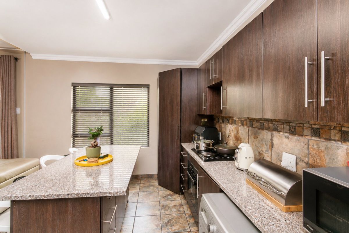 Modern kitchen featuring dark wood cabinetry, granite countertops, stone tile backsplash, and a functional breakfast island with integrated hob and oven.