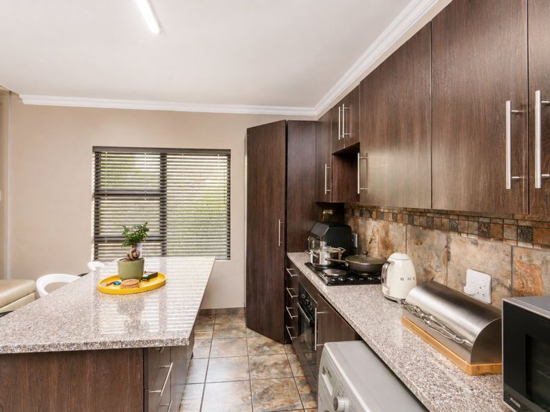 Modern kitchen featuring dark wood cabinetry, granite countertops, stone tile backsplash, and a functional breakfast island with integrated hob and oven.