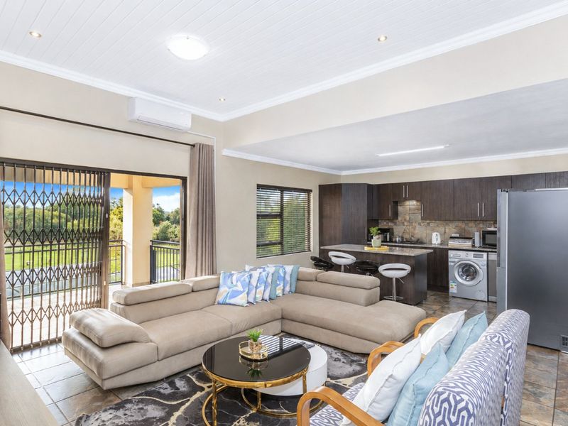 Spacious open-plan living area featuring a modern kitchen with dark cabinetry, stone countertops, and direct access to a private balcony through sliding security doors.