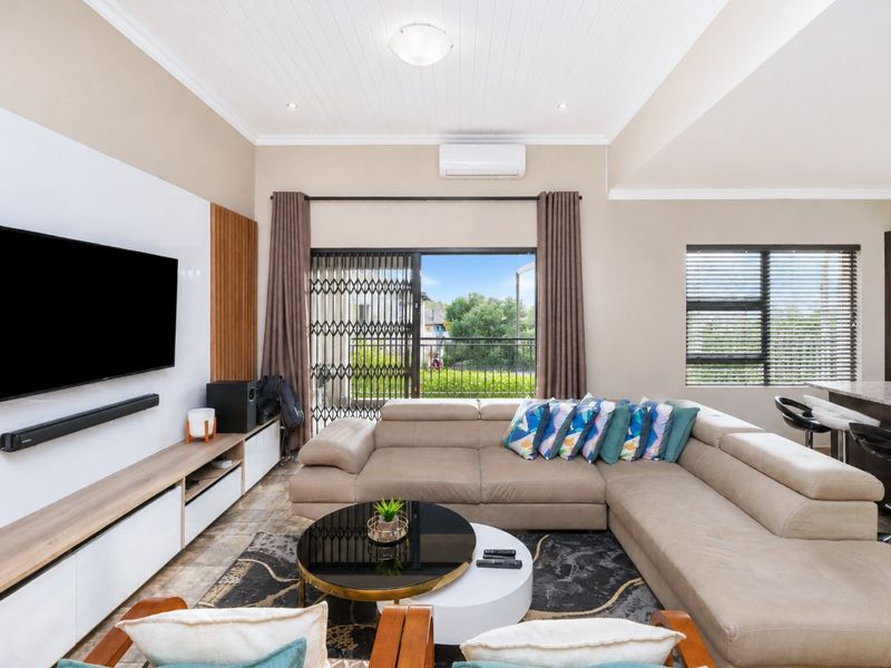 A bright open-plan living area featuring tiled floors, a built-in media unit, air conditioning, and direct access to a balcony through sliding glass doors.