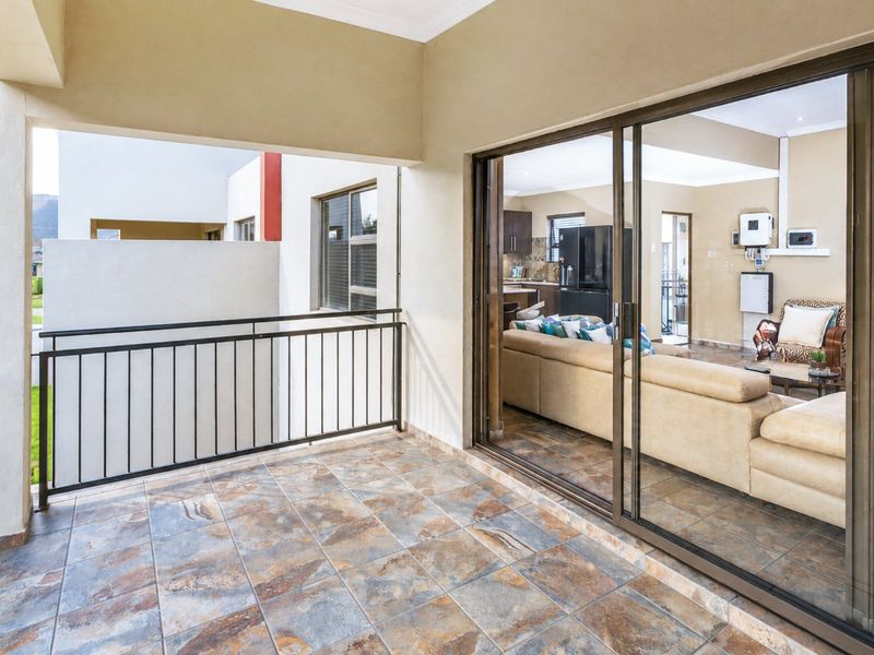 A covered balcony featuring tiled flooring and a metal balustrade, providing seamless access to the open-plan living area through large sliding glass doors.