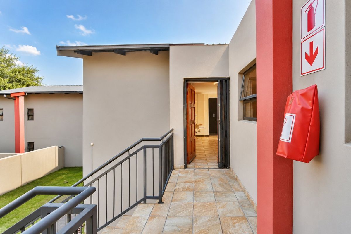 An exterior entrance landing featuring tiled flooring, a metal balustrade, and safety equipment, providing access to the apartment interior.
