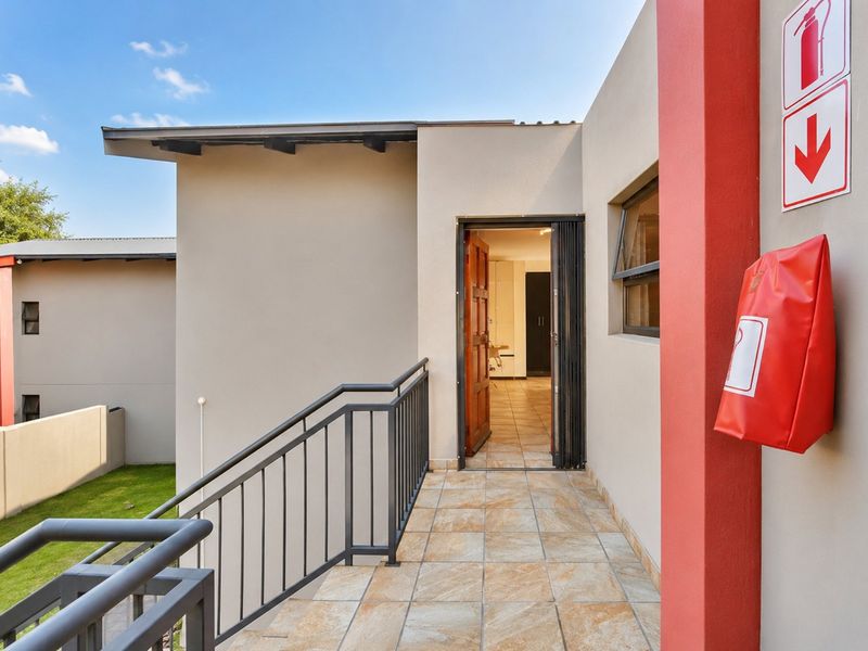 An exterior entrance landing featuring tiled flooring, a metal balustrade, and safety equipment, providing access to the apartment interior.