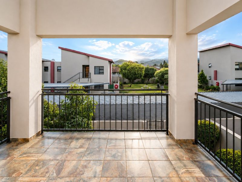 A spacious covered balcony featuring durable tiled flooring and a secure metal balustrade, offering pleasant views of the surrounding complex and landscape.