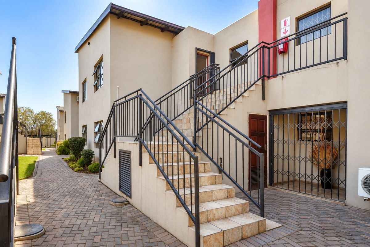 Exterior view of an apartment complex featuring a tiled staircase with metal railings, paved walkways, and secure access points.