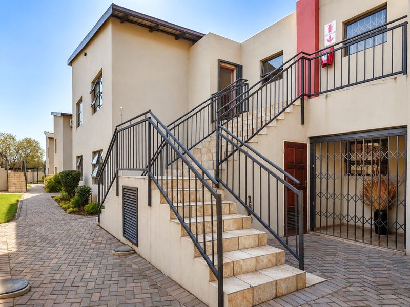 Exterior view of an apartment complex featuring a tiled staircase with metal railings, paved walkways, and secure access points.