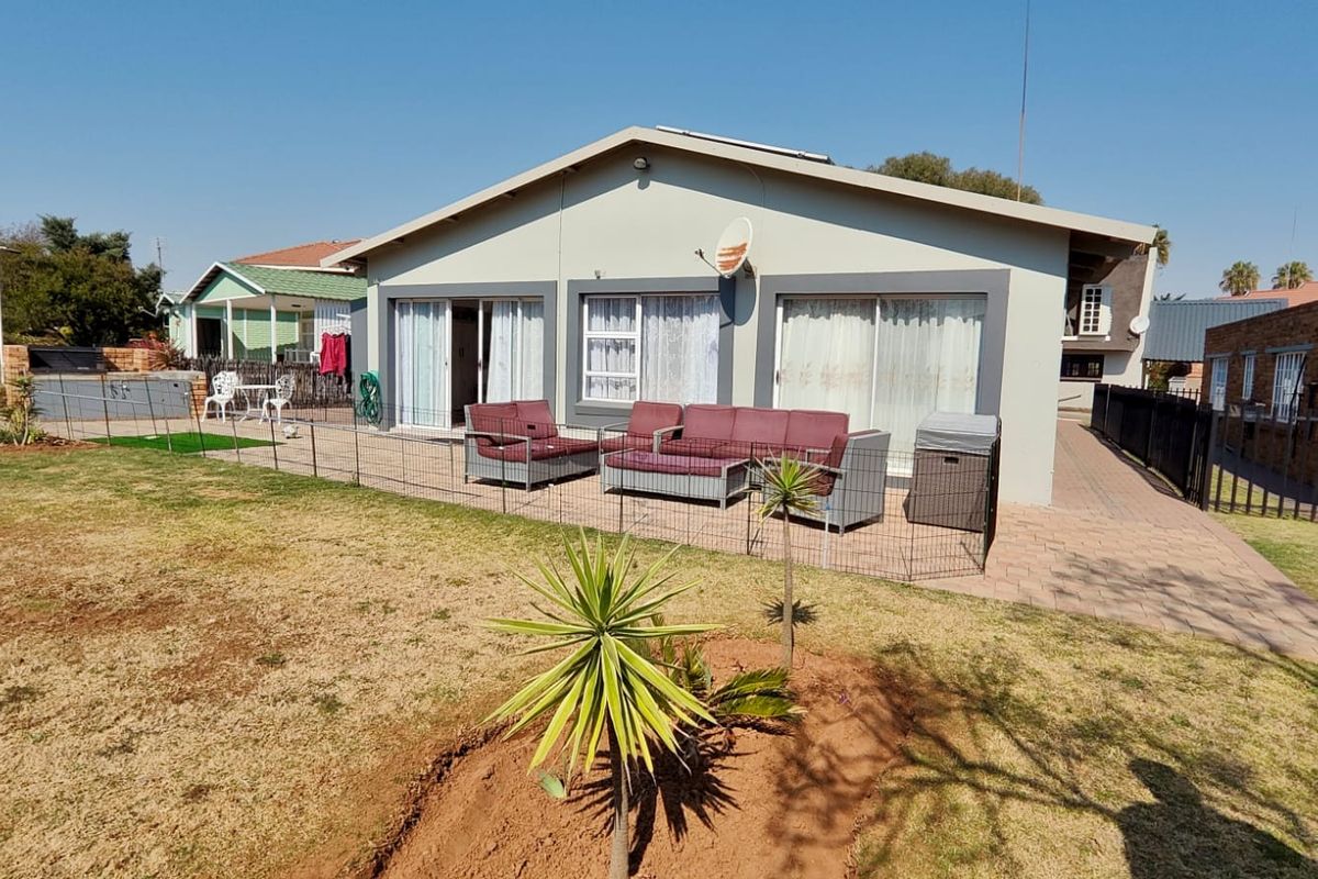 Rear view of the house featuring a paved patio area, sliding glass doors, and a spacious garden with established landscaping.