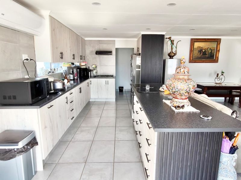 Modern open-plan kitchen featuring light wood-grain cabinetry, a large central island with dark countertops, tiled flooring, and integrated appliances.