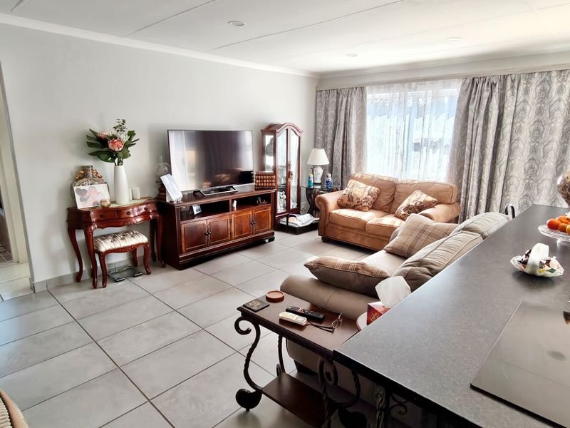 An open-plan living area featuring large format floor tiles, recessed lighting, and a kitchen island, with an adjacent view into a bathroom.
