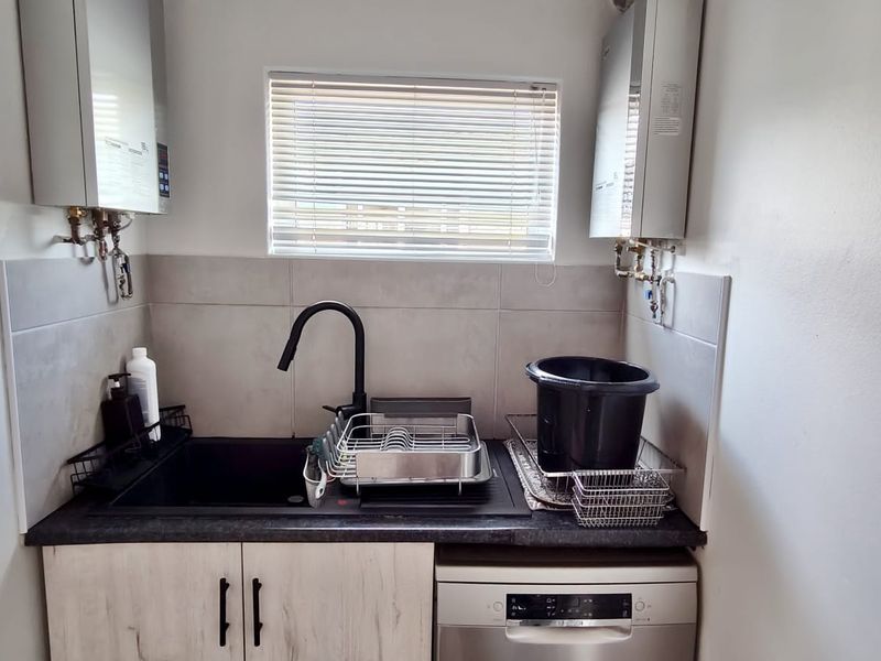 Compact scullery area featuring a modern black sink, gooseneck faucet, tiled backsplash, and dual gas geysers for efficient water heating.