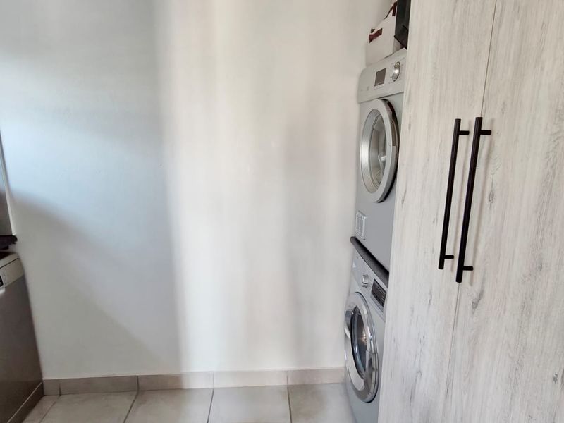 A functional laundry area featuring built-in cabinetry, tiled flooring, and space for stacked laundry appliances alongside an integrated dishwasher.