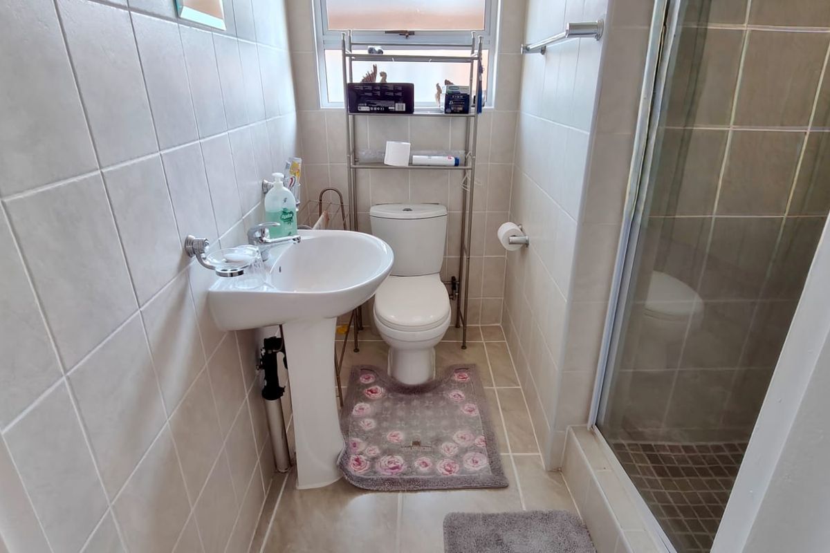 Compact bathroom featuring a pedestal basin, toilet, and a glass-enclosed shower with neutral wall and floor tiling.