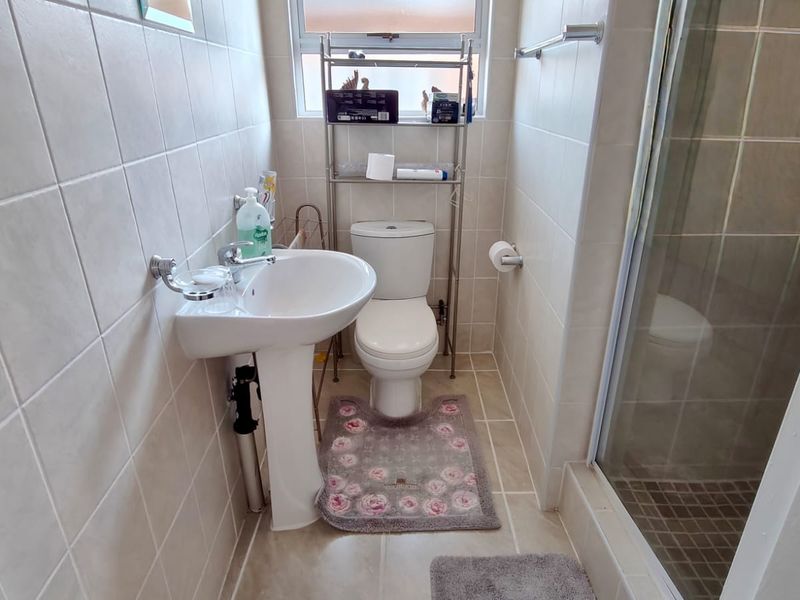 Compact bathroom featuring a pedestal basin, toilet, and a glass-enclosed shower with neutral wall and floor tiling.