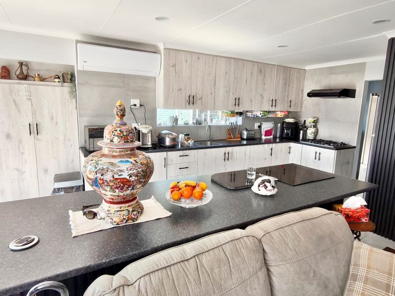Modern open-plan kitchen featuring light wood-grain cabinetry, a large central island with stone countertops, integrated gas hob, and split-system air conditioning.
