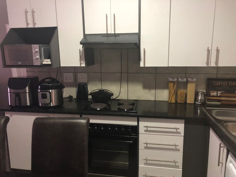 A functional kitchen featuring white cabinetry, dark granite countertops, a built-in oven with electric hob, and a tiled backsplash.