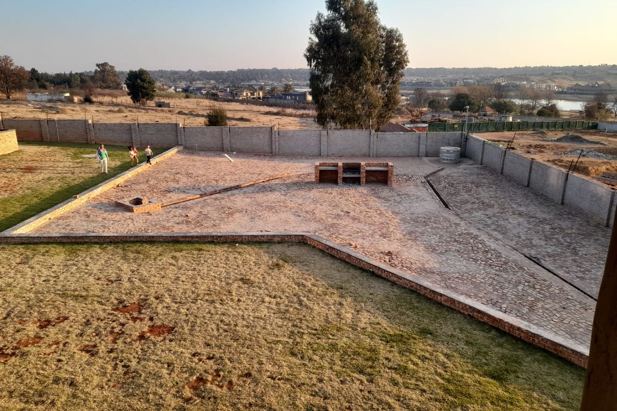 Spacious rear garden featuring a large paved area, built-in brick braai, and perimeter walling with views of the surrounding landscape.