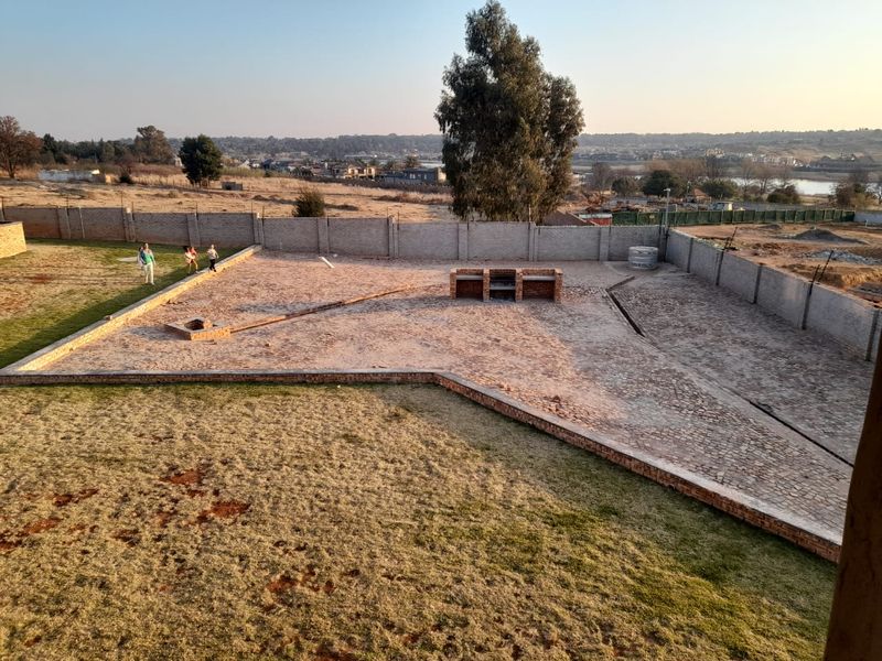 Spacious rear garden featuring a large paved area, built-in brick braai, and perimeter walling with views of the surrounding landscape.