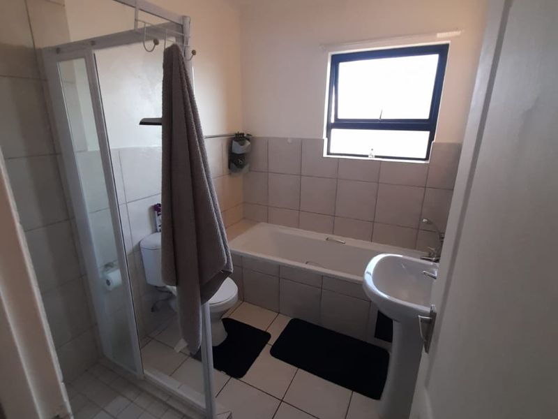 A functional bathroom featuring a separate shower enclosure, bathtub, pedestal basin, and toilet with neutral wall and floor tiling.