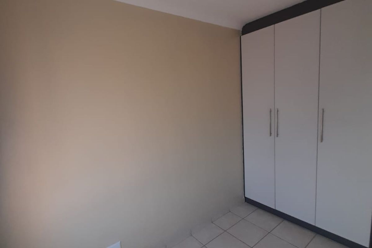 A clean, empty bedroom featuring neutral wall tones, tiled flooring, and a functional built-in wardrobe with modern finishes.