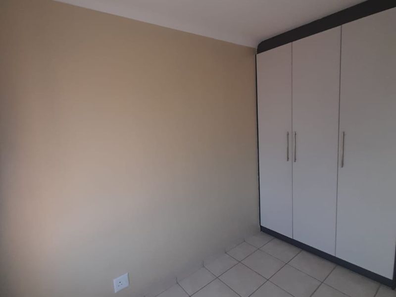 A clean, empty bedroom featuring neutral wall tones, tiled flooring, and a functional built-in wardrobe with modern finishes.