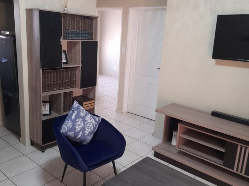 A living room area featuring neutral wall tones, tiled flooring, and coved ceiling details, providing a functional space with access to adjacent rooms.