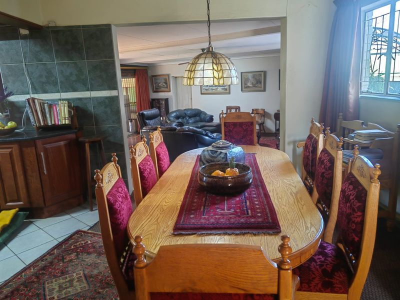 Open-plan dining area featuring tiled floors and a pendant light, flowing into a kitchen space with built-in cabinetry and a tiled backsplash.