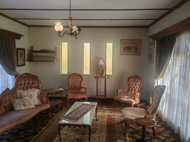 A traditional living room featuring vertical clerestory windows, an exposed beam ceiling, and a classic chandelier, offering a dated but well-maintained interior space.
