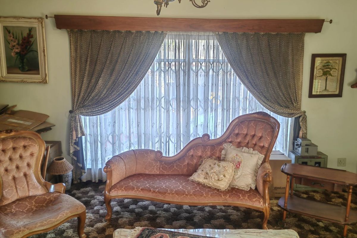 A traditional living room featuring a large window with a decorative timber pelmet, security gate, and classic chandelier lighting.