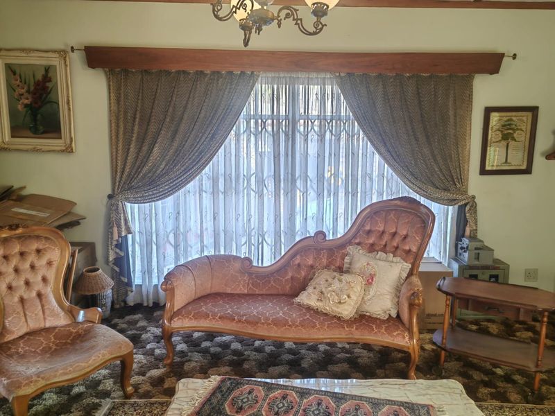 A traditional living room featuring a large window with a decorative timber pelmet, security gate, and classic chandelier lighting.