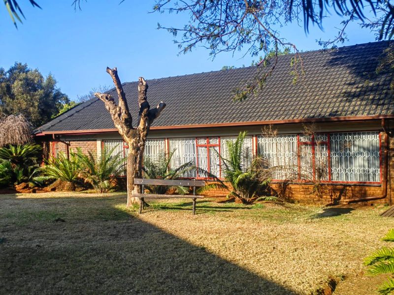 Rear view of a single-story brick house featuring a tiled roof and security-barred windows overlooking a garden area.