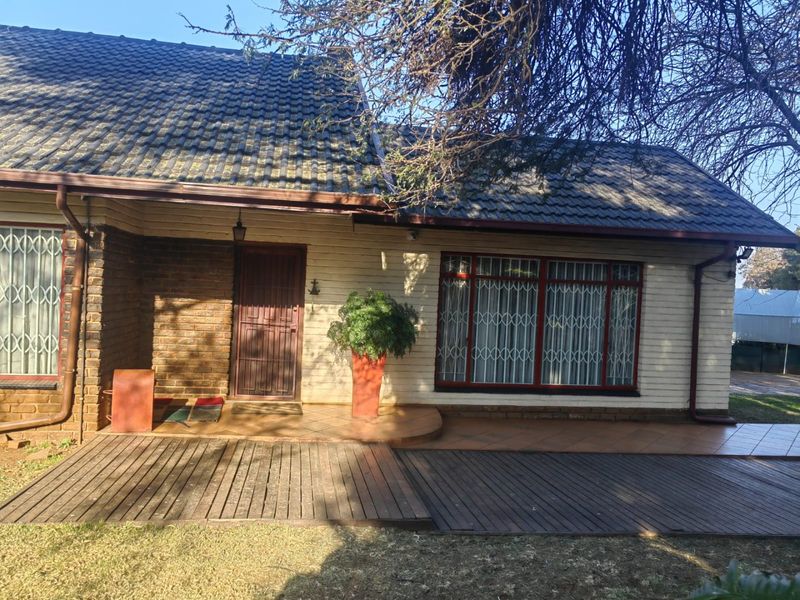 Front facade of a house featuring a tiled roof, brick and painted siding, a tiled patio area, and timber decking.
