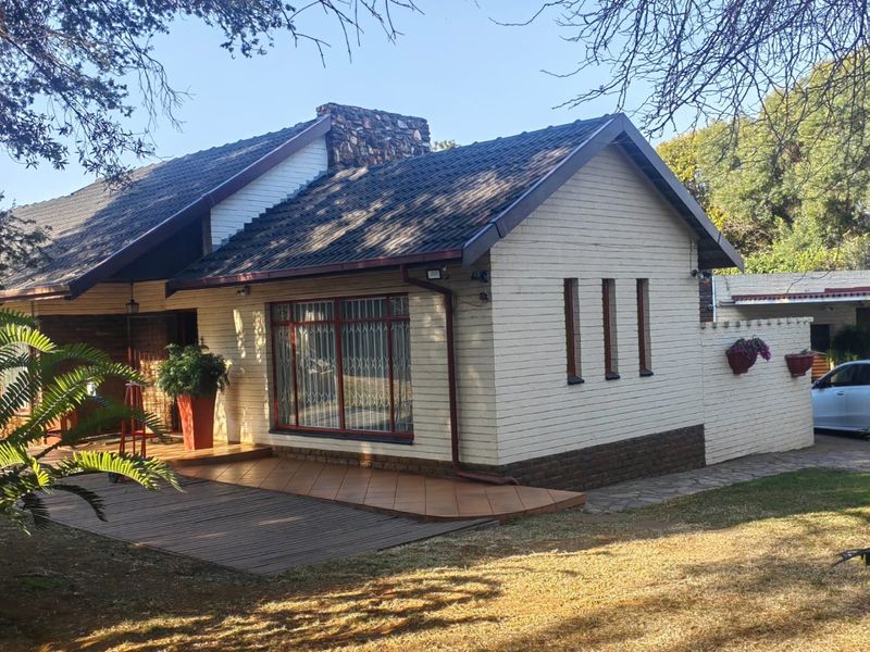 Front elevation of a brick house featuring a stone chimney, tiled roof, security-barred windows, and a combination of tiled patio and wooden decking.