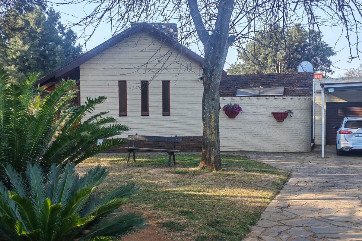Rear view of the property featuring a brick facade, paved driveway, and attached garage area with established garden surroundings.