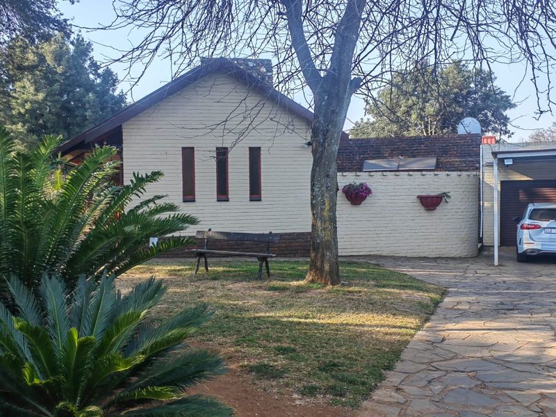 Rear view of the property featuring a brick facade, paved driveway, and attached garage area with established garden surroundings.