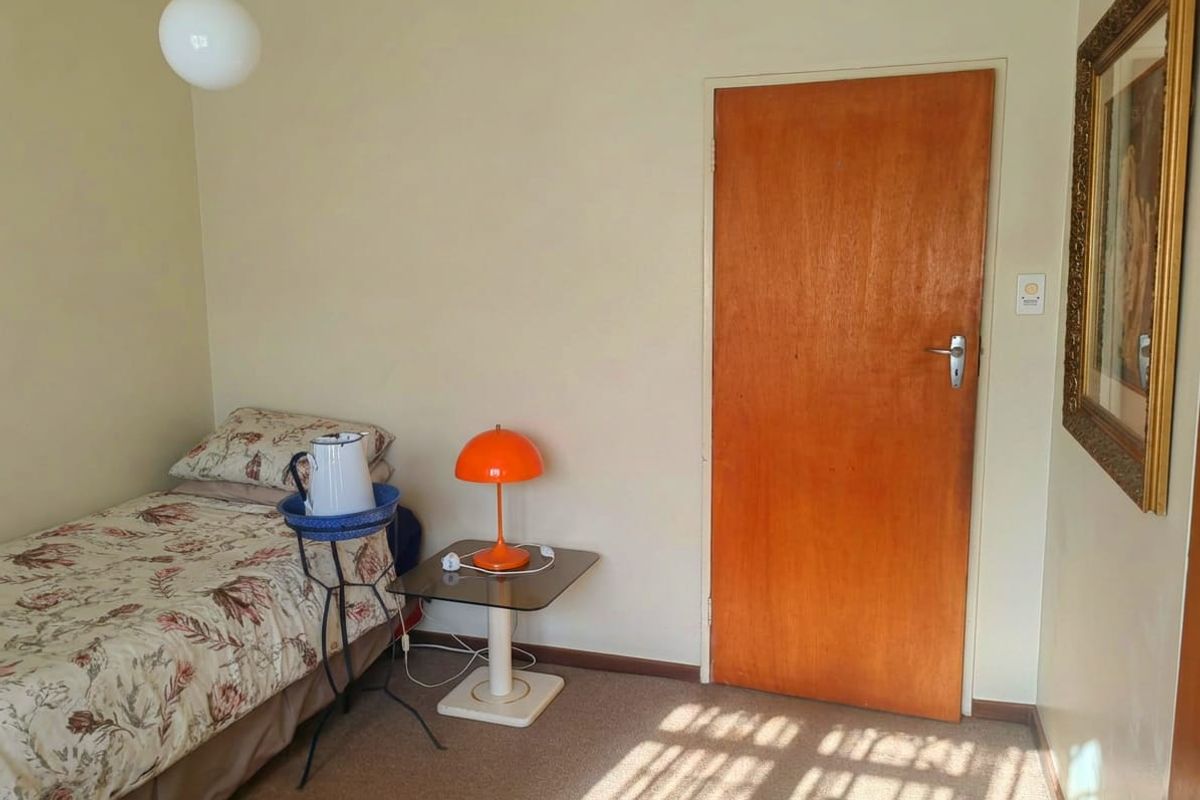 A standard bedroom featuring carpeted flooring, a wooden door, and a simple pendant light fixture.