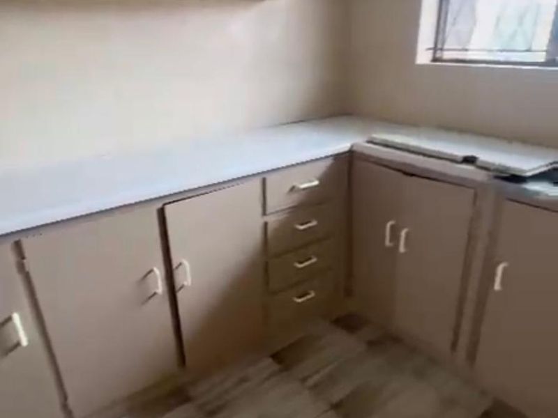 A dated, empty kitchen featuring laminate cabinetry, tiled flooring, and a window with security bars, offering potential for a modern renovation.