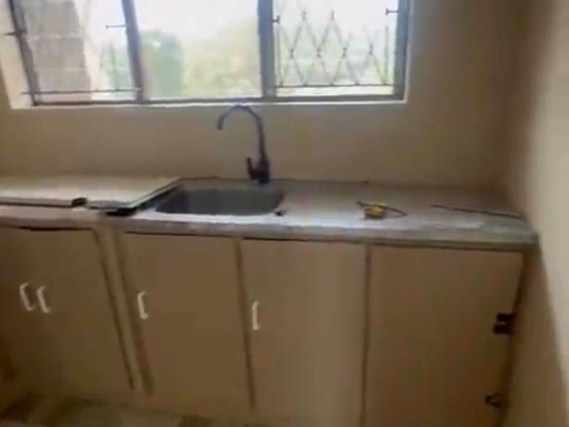 A compact, dated kitchen area featuring basic cabinetry, a single sink, and a window with security bars, requiring modernization and cosmetic updates.