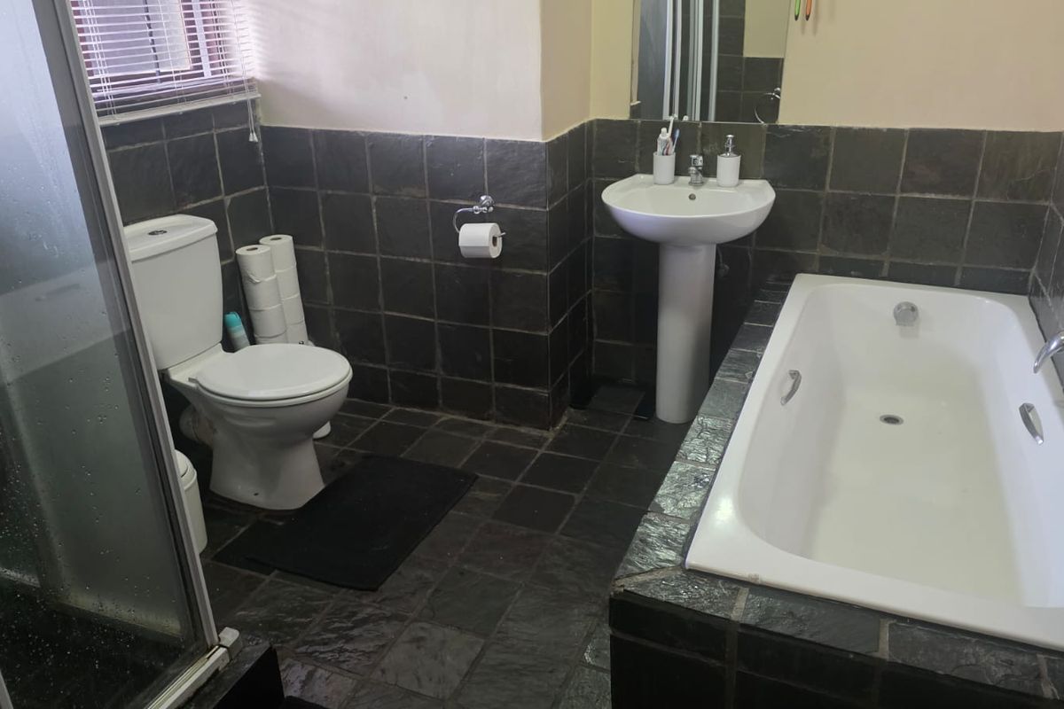 A functional bathroom featuring a pedestal basin, built-in bathtub, separate shower enclosure, and dark slate tile finishes throughout.