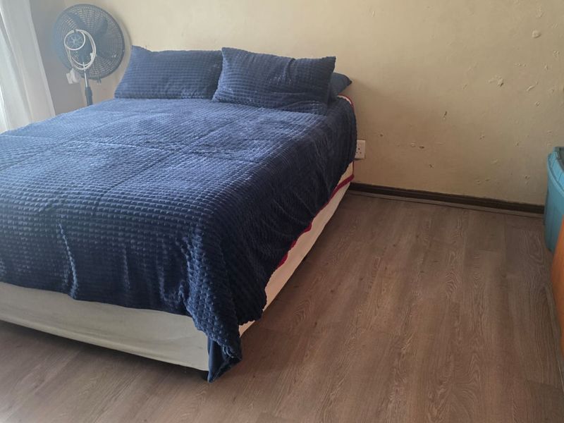 A bedroom featuring laminate flooring and visible wall surface damage, requiring cosmetic attention to improve the overall condition of the space.