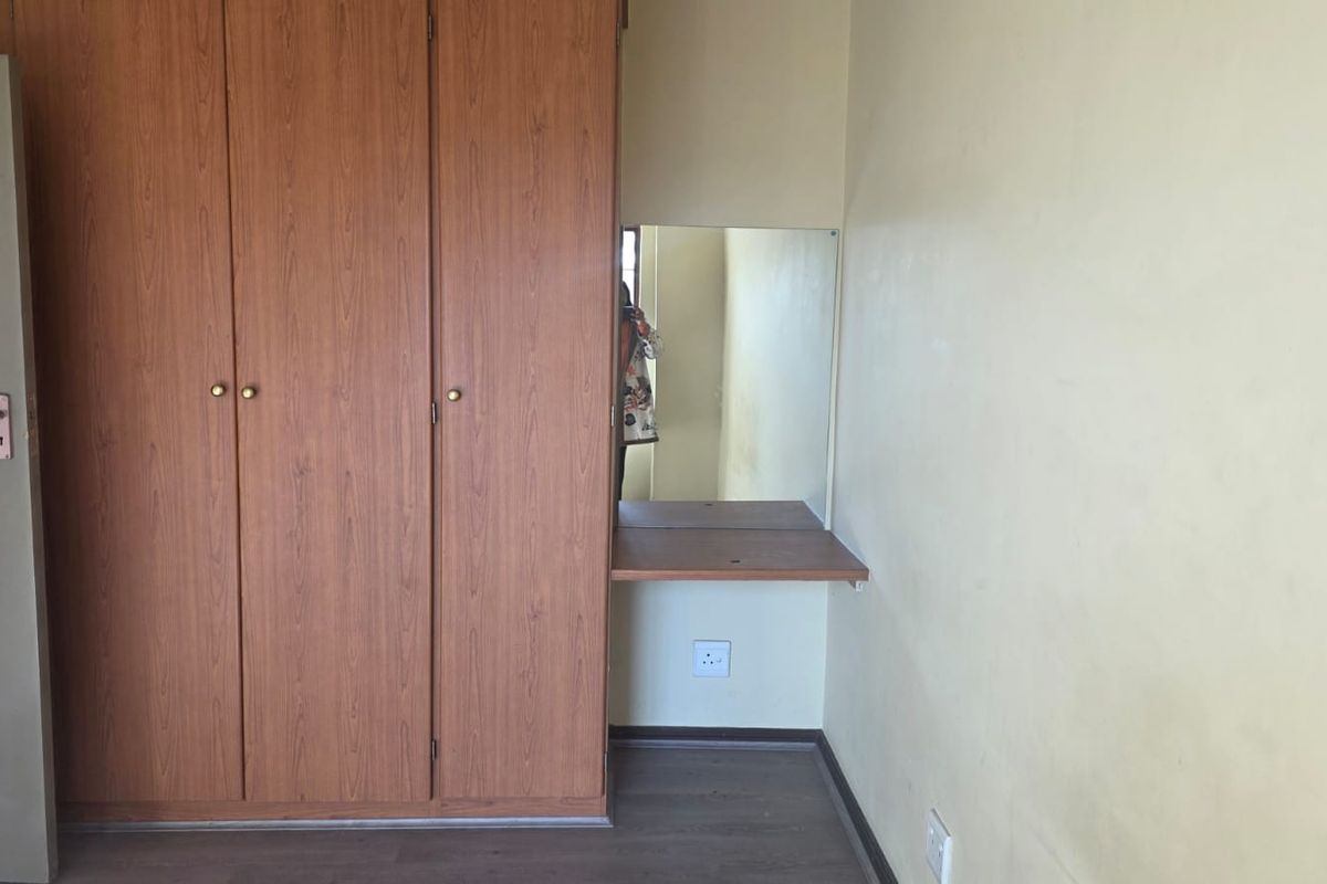 A bedroom featuring a built-in wooden wardrobe with an integrated vanity mirror and shelf, finished with laminate flooring.