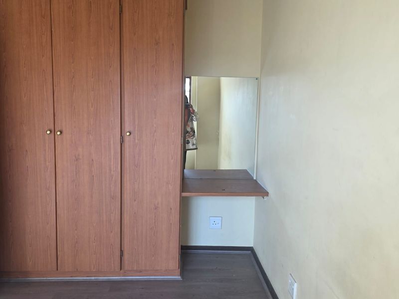 A bedroom featuring a built-in wooden wardrobe with an integrated vanity mirror and shelf, finished with laminate flooring.