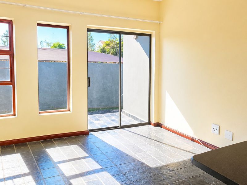 An empty open-plan living area featuring tiled flooring, large windows, and a sliding glass door providing access to an outdoor space.