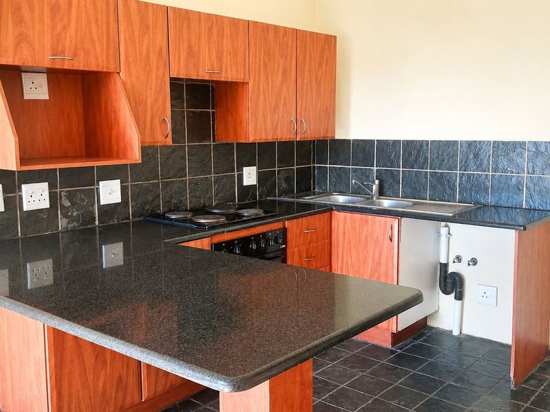 A functional kitchen featuring wood-look cabinetry, granite countertops, a built-in oven and hob, and a tiled backsplash.