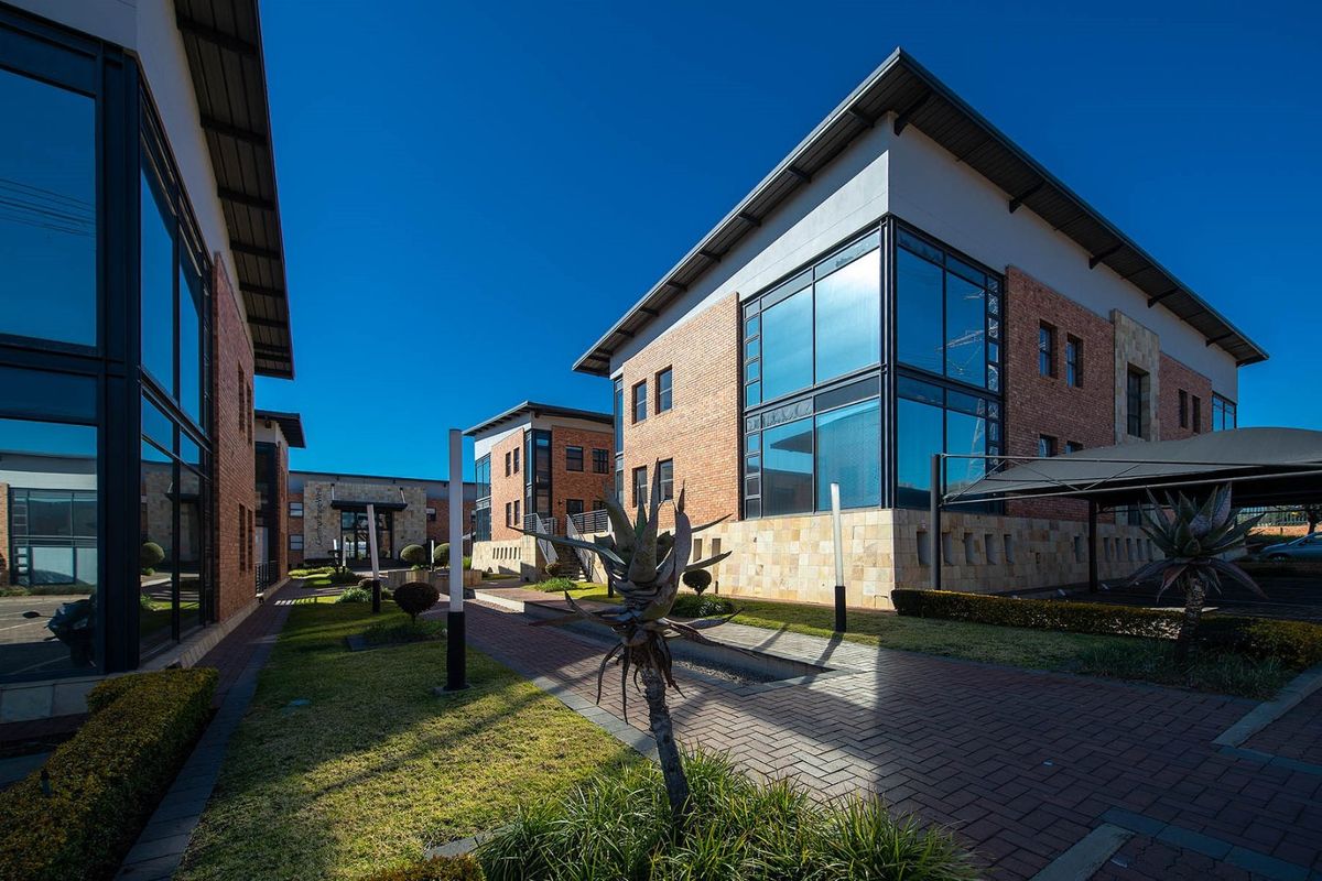 Modern commercial office complex featuring brick and stone facades, large glass windows, paved walkways, and landscaped grounds with integrated carports.